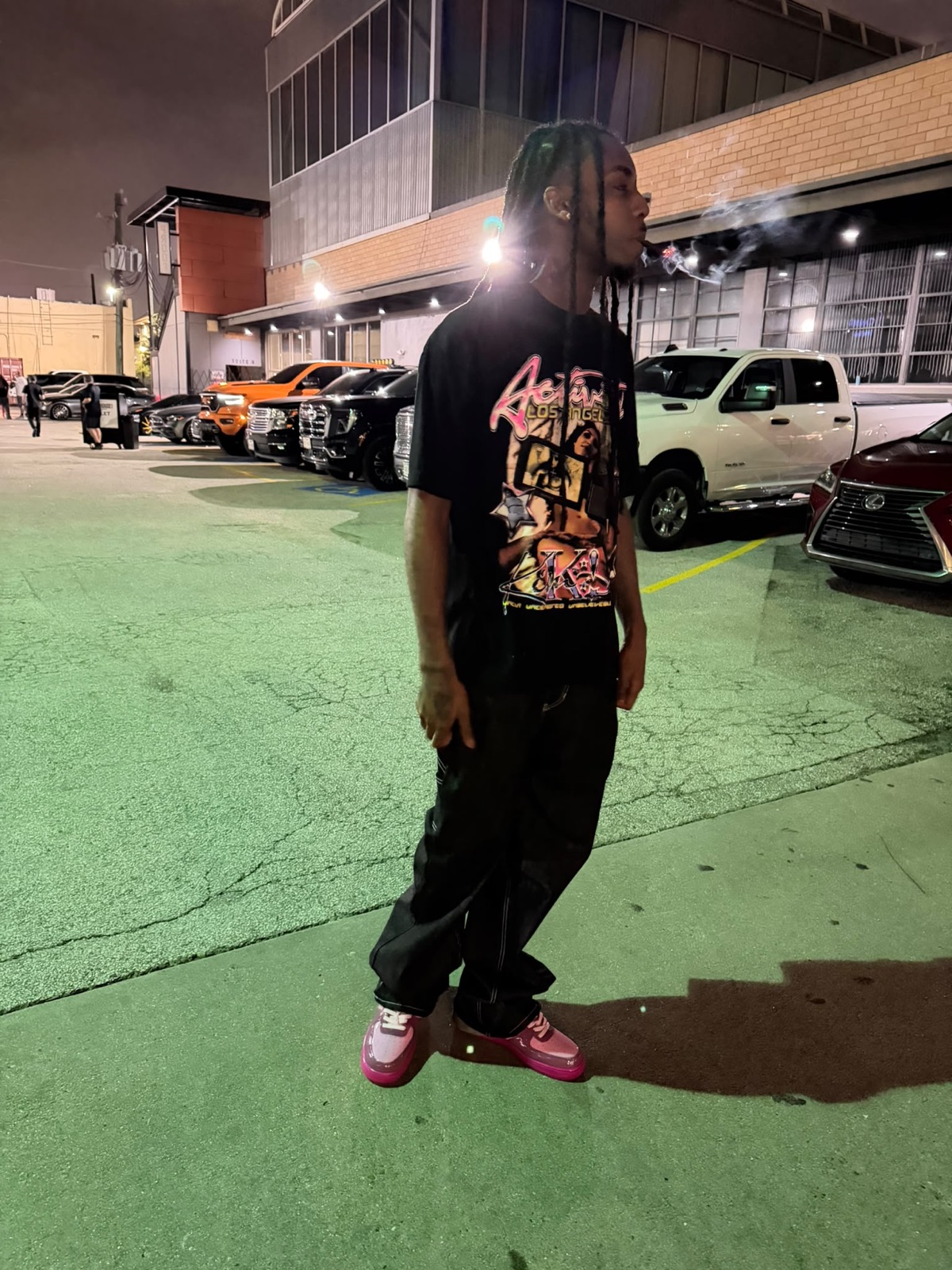 FMR Trill exhaling smoke in a lit-up parking lot at night